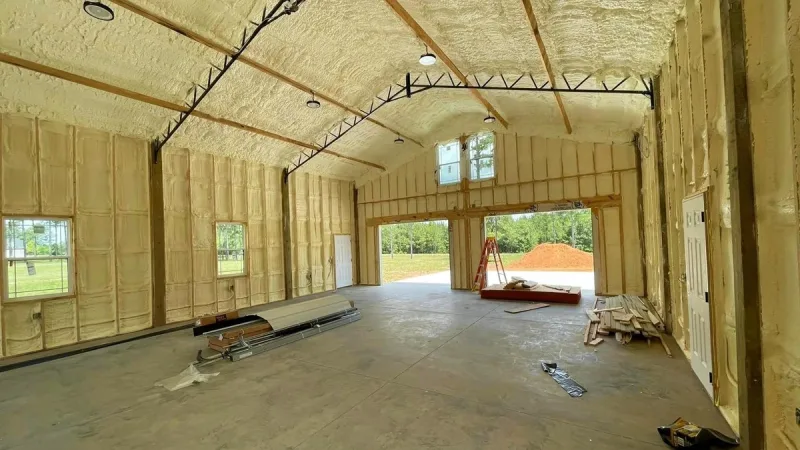 Interior of a post-frame building with spray foam over the roof deck and wall panels between the girts